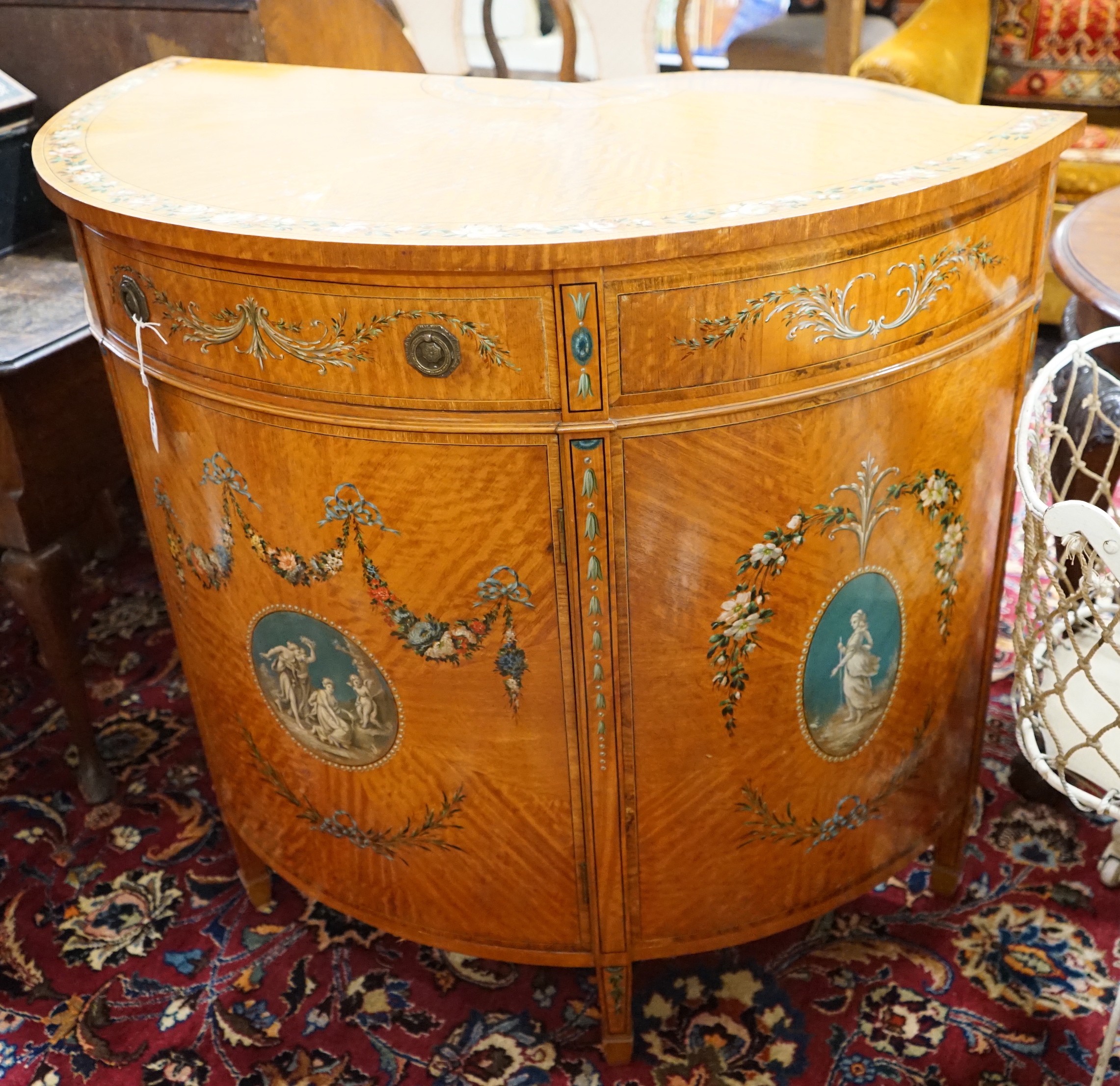 An Edwardian Sheraton revival painted satinwood demi lune side cabinet, width 107cm, depth 52cm, height 93cm
